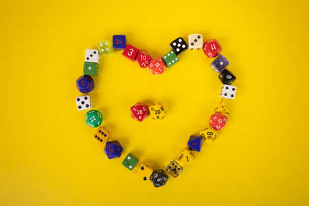 Random colorful dice in a heart shape on a bright yellow background flat layの写真素材