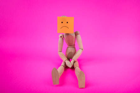 Wooden manikin doll sitting shoulders hunched over sulking sad face sign on the figures faceの写真素材