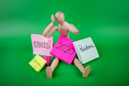 Wooden jointed manikin doll sitting hands on head sad and sulking with signs year 2020 pandemic...