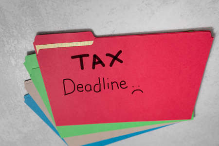 Tax Deadline Handwritten on red office file folder with sad face frowningの写真素材