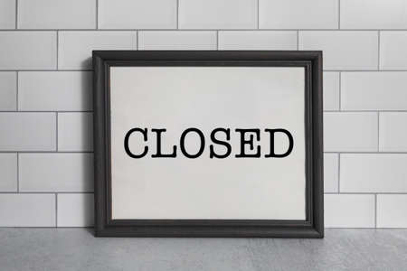 Closed signage on white paper in a black picture frame on white subway tile wallの写真素材