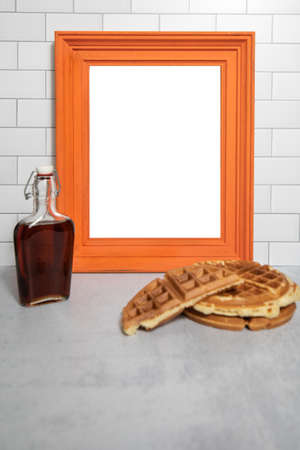 Blank empty white poster orange wooden frame with sweet maple syrup and stacked breakfast wafflesの写真素材