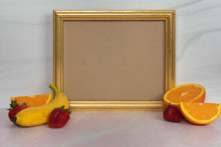Gold picture frame empty no words fruit on the sides bananas whole strawberries oranges halved and slicedの写真素材