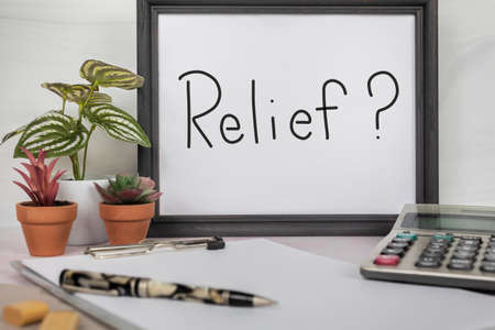 The word Relief handwritten on a white sign in dark gray picture frame sitting on home office study desk with calculator pen and clipboardの写真素材
