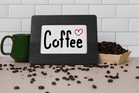 Sign with the word Coffee handwritten with red heart on white paper in a black picture frame whole coffee beans in the background and tea cupの写真素材