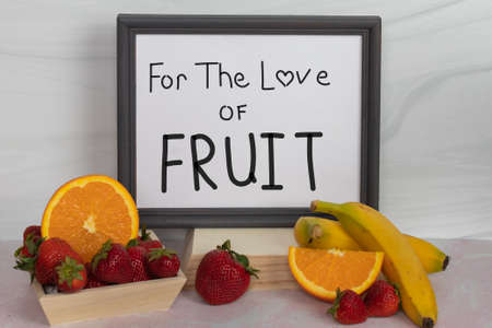For The Love Of Fruit white sign in gray picture frame assorted sweet fresh raw fruits yellow bananas whole strawberries halved and sliced navel orangesの写真素材