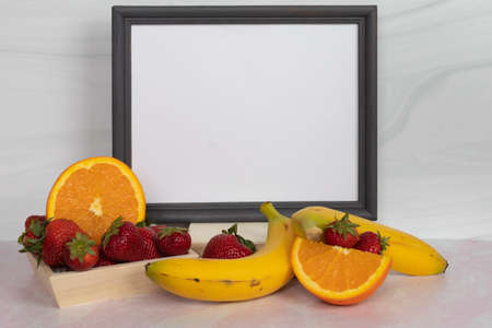 Dark gray picture frame empty white blank sign with fruit in the  foreground strawberries bananas and naval orangesの写真素材