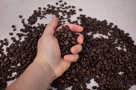Real person hand holding a hand full of whole roasted coffee beans scattered coffee beans in the backgroundの写真素材