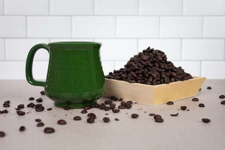 Green ceramic coffee mug with handle sitting next to wood bowl of piled whole dark roasted coffee beansの写真素材