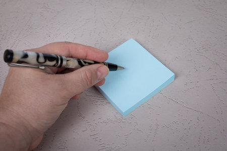 Real human person hand holding a pen about to write on light blue square posted notepadの写真素材