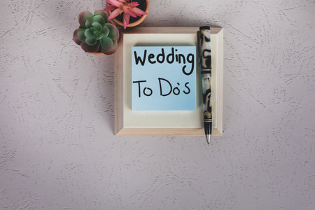 wedding preparation to do lists Wedding To Do's handwritten on square light blue posted notepad with pen and office desk plantsの写真素材