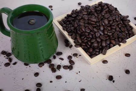 close up of green ceramic coffee cup filled with hot brewed coffee wood bowl of coffee beans scattered dark roasted whole coffee beansの写真素材
