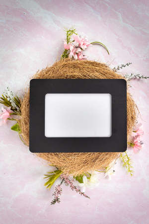 Blank empty black picture frame laying flat in a bird nest with spring greenery pink and white flowers no words ready to add your message or contentの写真素材