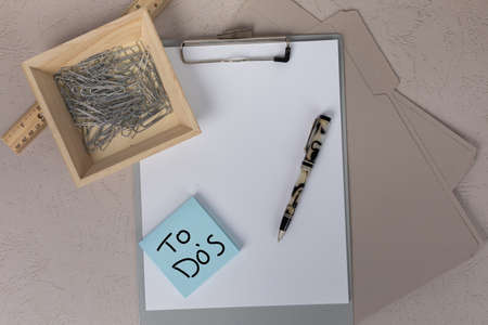 To Do's handwritten message on a square posted sticky notepad with a office clipboard pen and paperclips ing the background office workspaceの写真素材