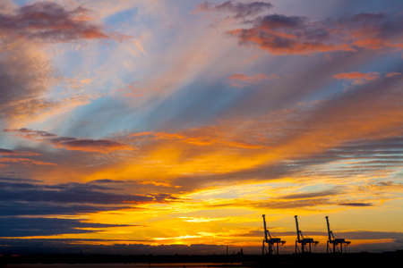 Port cranes silhouettes in beautiful golden glowing sunset in Melbourne, Australiaの写真素材