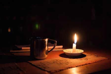 Cup and burning candle on wooden table in the dark.の写真素材