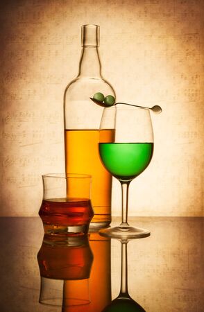 Still life composition with glasses and bottle filled with colored liquids on light textured backgroundの写真素材