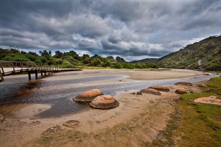 Wooden footbridge across Tidal River on stormy weather. Wilsons Promontory, Victoria, Australiaの写真素材