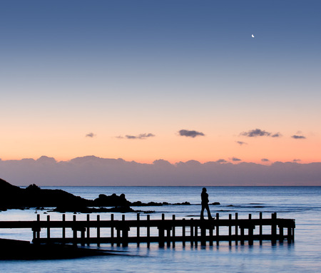 Silhouette of a woman walking on pier with moon in the skyの写真素材