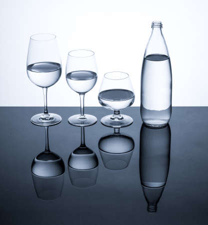 Glassware and bottle filled with water on white backgroundの写真素材