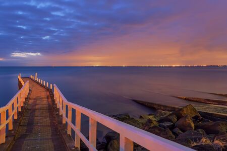 Small Jetty leading into the sunset with distant city lights of Melbourne CBD.の写真素材