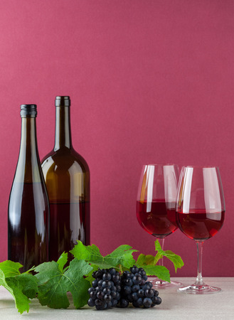 Two red wine bottles and glasses with ripe grapes on marble and red backgroundの写真素材