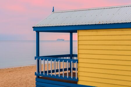 Yellow beach hut overlooking a cruise liner sailing across the water at pink sunriseの写真素材