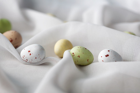 Chocolate speckled Easter eggs in crisp sugar shell among delicate white gauze fabric folds that looks like milk. Shallow depth of field.の写真素材