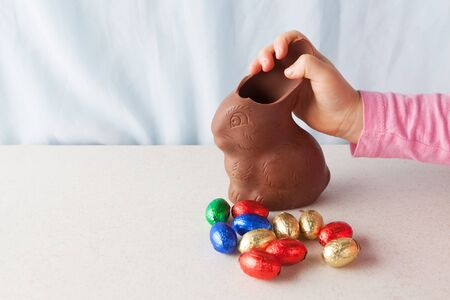 Child's hand breaking an ear off chocolate Easter bunny with copy space.の写真素材