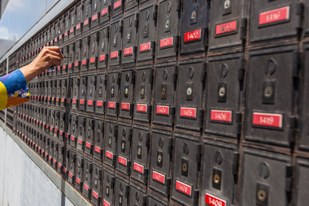 Woman hand holding a key and unlocking a PO box, in the long row of PO boxesの写真素材
