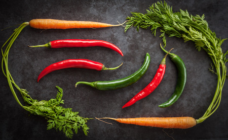 Hot chilli peppers and Dutch sweet carrots creatively arranged on grunge background. Top view.