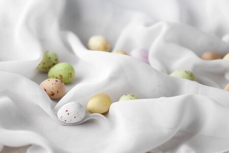 Chocolate speckled Easter eggs in crisp sugar shell among delicate white gauze fabric folds that...