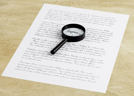 Magnifying glass enlarging the word Happiness on a page with printed text laying on a desktop