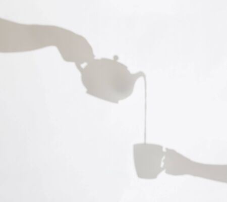 Delicate shadows of teapot pouring liquid into a cup held by female hand. Shadow play.の写真素材