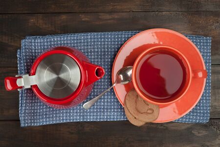 Breakfast tea composition with red teapot, teacup with saucer and cookies on towel and wooden table. Top view.の写真素材