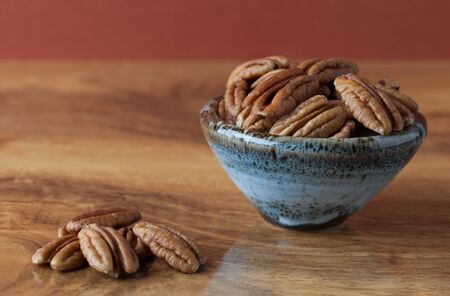 Pecans on wooden table and in ceramic bowl with brown background. Copy space, shallow depth of fieldの写真素材