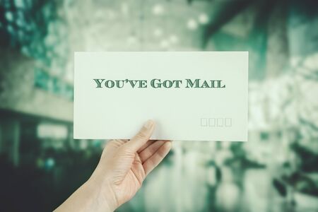 Female hand delivering a postage envelope on blurred urban background. Image has vintage filter appliedの写真素材