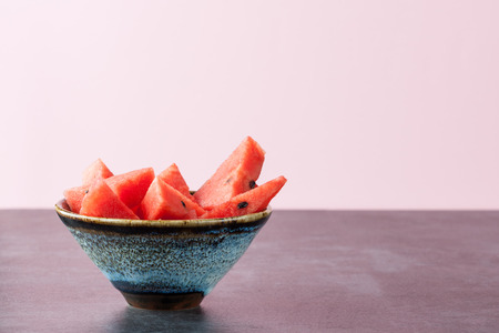 Triangle shaped watermelon slices placed in ceramic bowl on dark grungy surface with copy space. Shallow depth of field.の写真素材