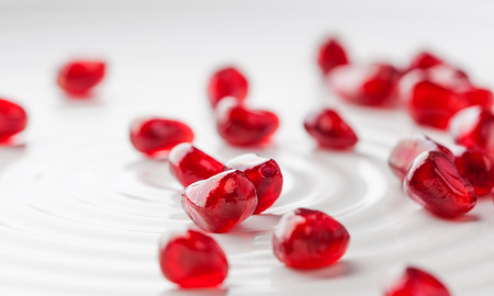 Pomegranate seeds scattered on elegant white plate with back lighting. Shallow depth of fieldの写真素材