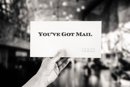 Female hand delivering a postage envelope on blurred urban background in black and whiteの写真素材