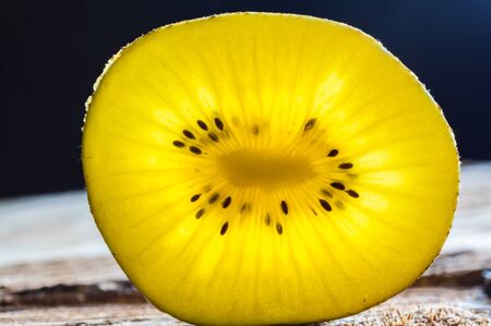 Closeup of yellow kiwi slice glowing with translucent light on rough wooden surfaceの写真素材