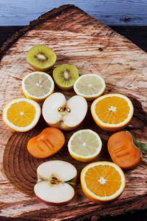 Slices of various fruits on freshly cut wooden stump. Kiwi, orange, apple, lemon, and persimmonの写真素材