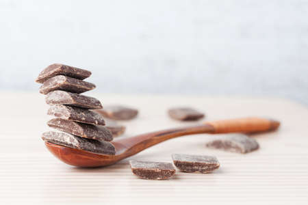 Dark cooking chocolate chunks placed on top of eachother on wooden spoon with copy spaceの写真素材