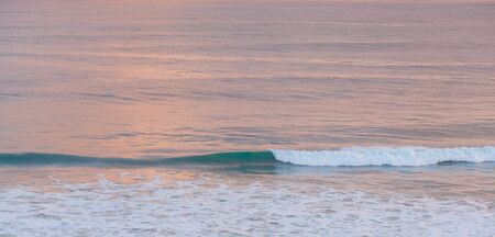 Breaking turquoise ocean wave closeup at pink sunset