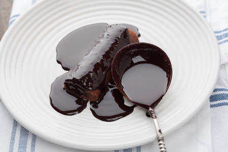 Closeup of sweet tube covered in dark melted chocolate with vintage silver spoon on white plateの写真素材