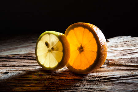 Slices of orange and lemon glowing with translucent light on rough wooden surfaceの写真素材