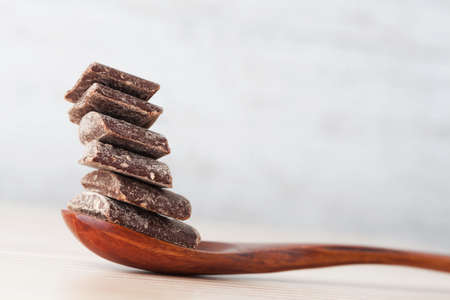 Dark cooking chocolate chunks placed on top of eachother on wooden spoon with copy spaceの写真素材