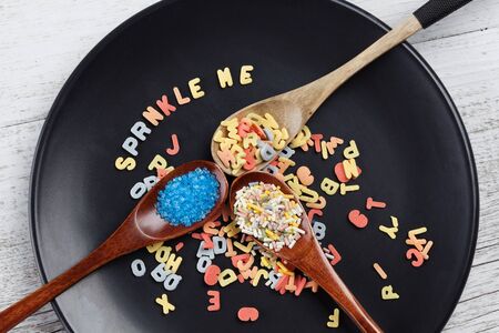 Colorful sugar sprinkles in wooden spoons on black plate. Top view horizontal imageの写真素材