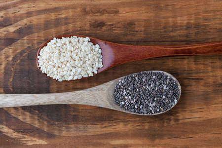 Sesame seeds and black chia seeds in wooden spoons top viewの写真素材