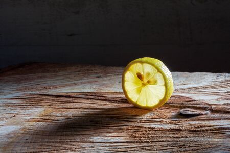 Slice of lemon glowing in translucent light on rough wooden surface with copy spaceの写真素材